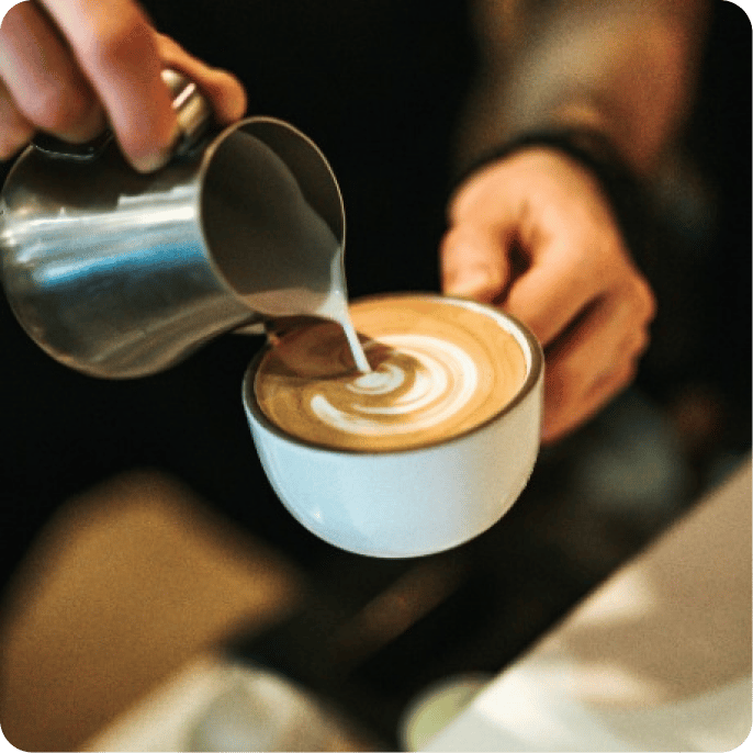 a person serving milk over the coffee making a figure with it
